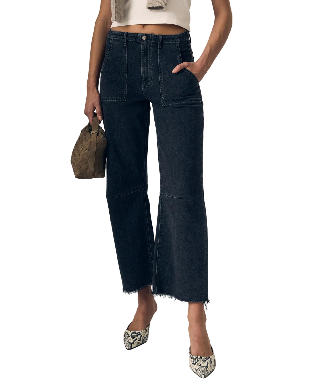 Person wearing faded black jeans and a white top, holding a small bag on a plain background
