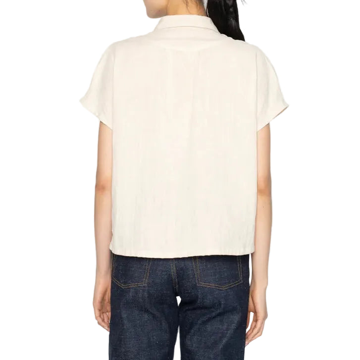 Person wearing a cream-colored short-sleeve shirt and dark jeans on a white background