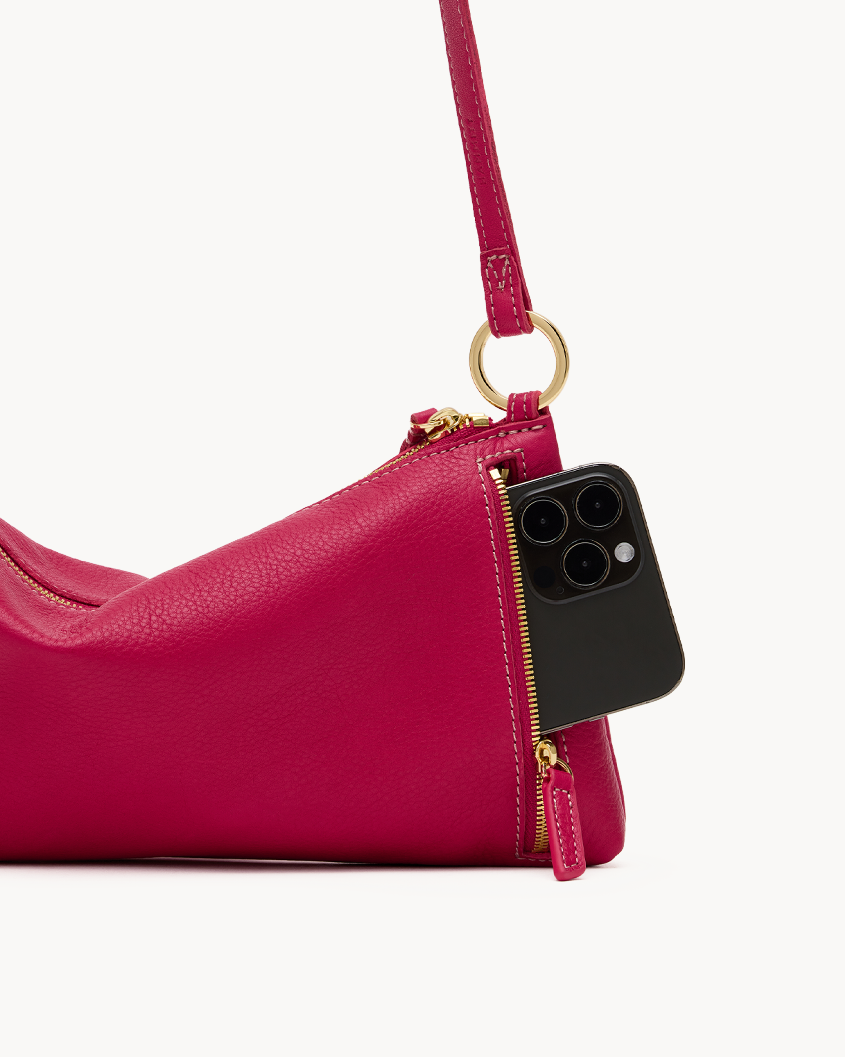 Close up of a phone pocket of a magenta leather convertible bag with gold accents on a white background