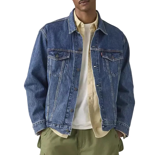 Man wearing a blue denim jacket, beige shirt, and green pants on a light gray background