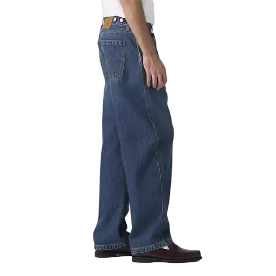 Person wearing a white t-shirt, blue jeans, and a navy cap on a plain background
