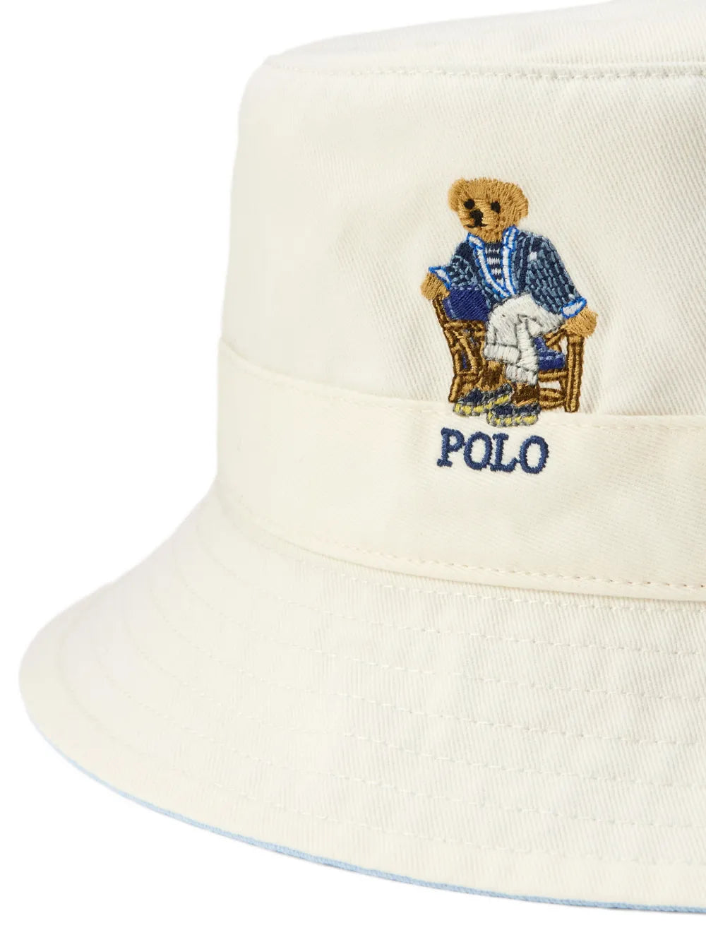 Close up of a white bucket hat with an embroidered bear logo on a white background