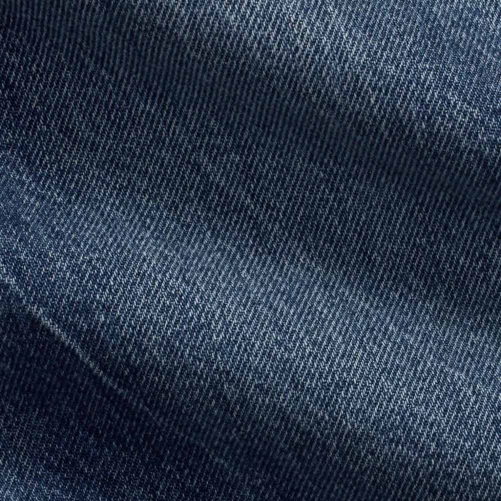 A close-up of dark blue denim fabric with visible twill texture and soft folds.
