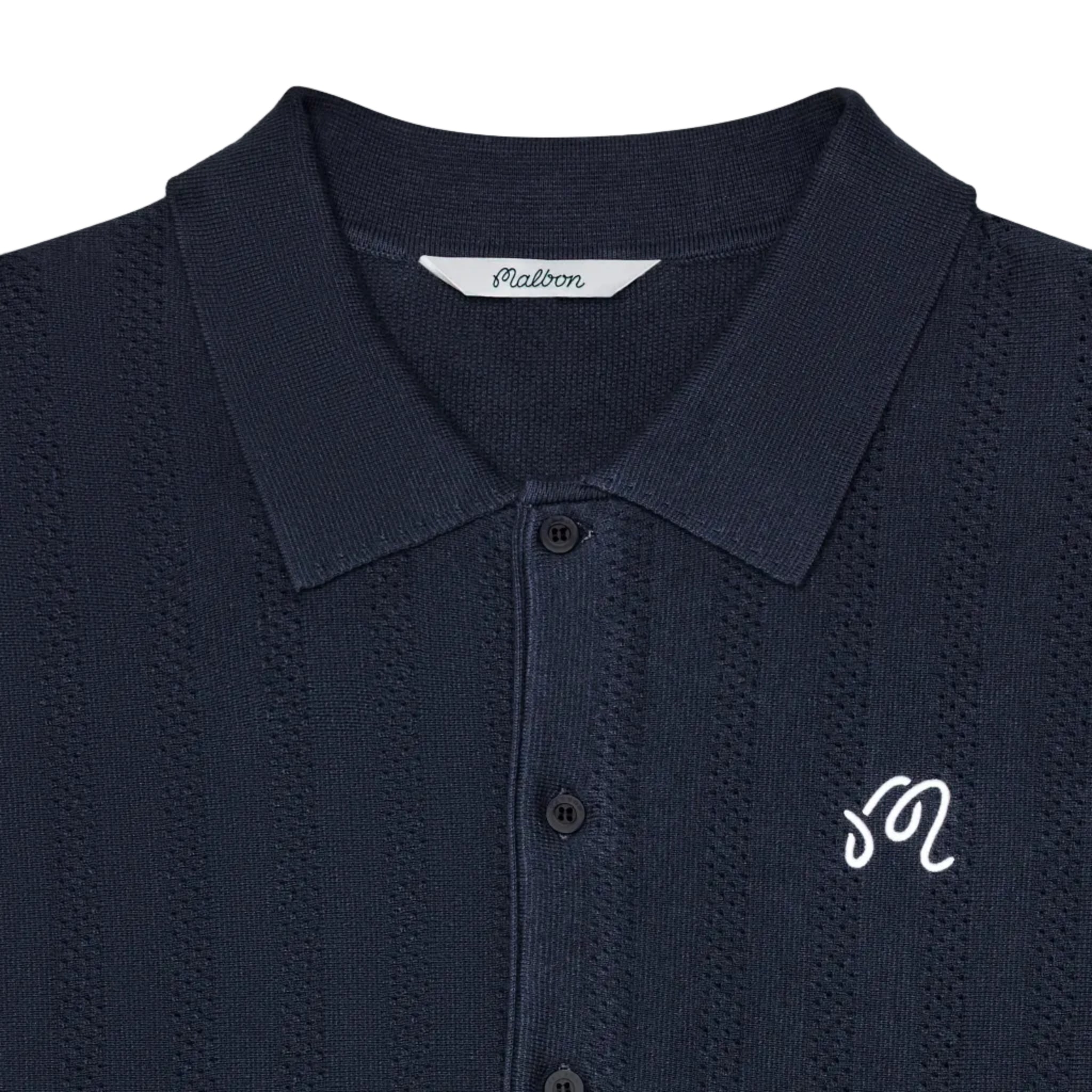 Close-up of a dark navy blue textured knit polo shirt with a white embroidered script logo on the chest and a visible 'Malbon' brand label inside the collar.