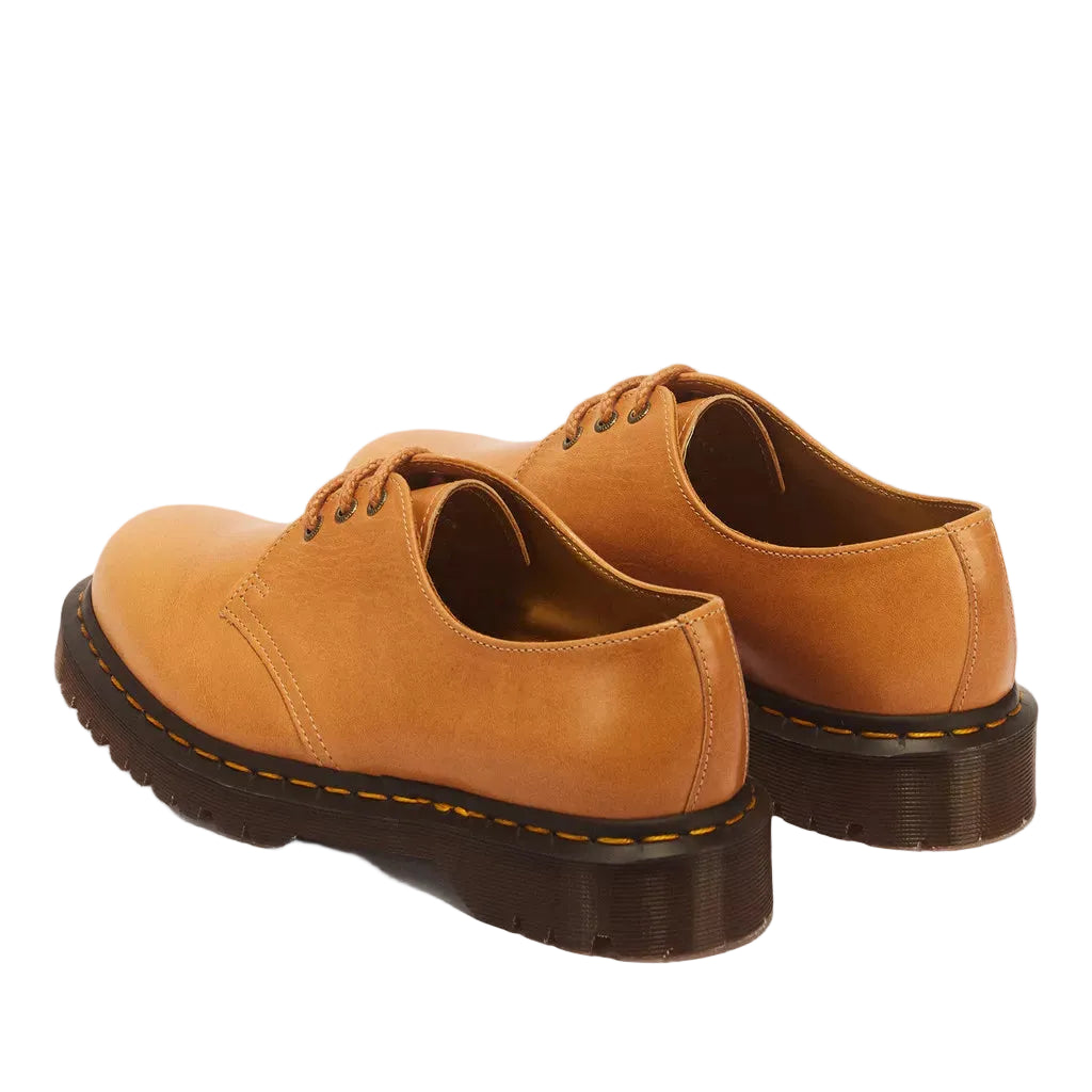 A pair of tan leather lace-up shoes with dark brown soles, shown from a three-quarters rear angle on a light gray background.
