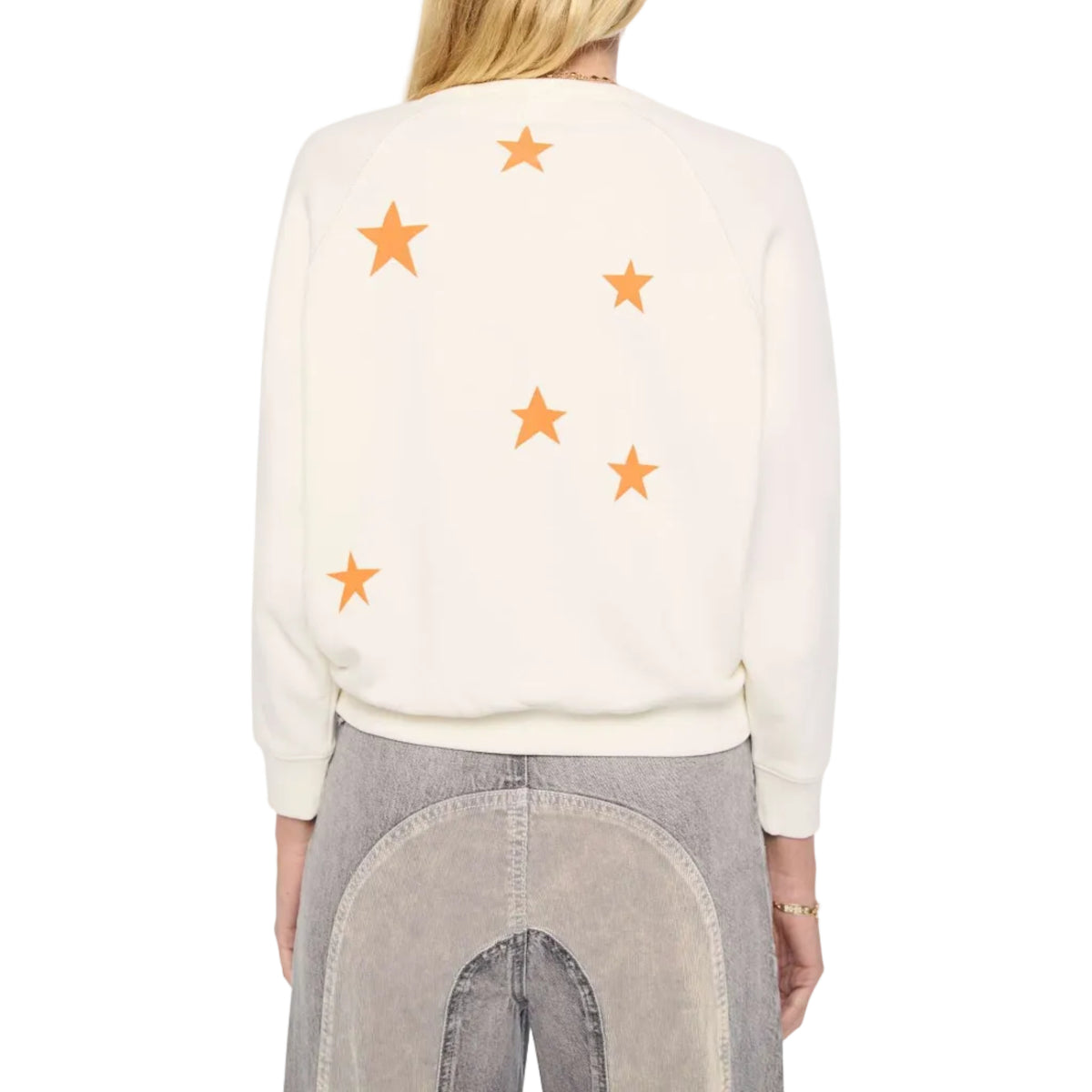 A woman viewed from the back wearing a cream-colored crewneck sweatshirt with orange embroidered stars, paired with gray patchwork jeans, against a plain white background.
