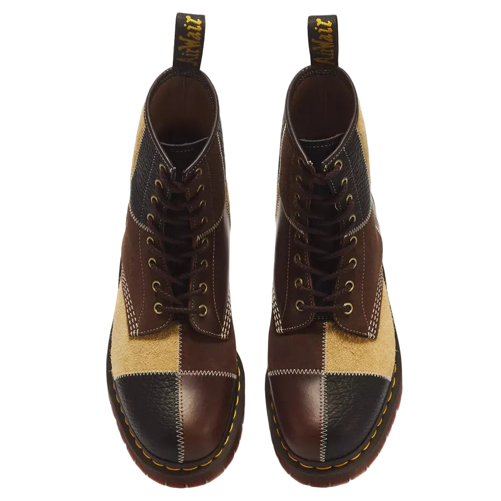 A pair of Dr. Martens lace-up ankle boots featuring a patchwork design of dark brown leather, tan suede, and black leather panels, shown from a top-down view on a white background.