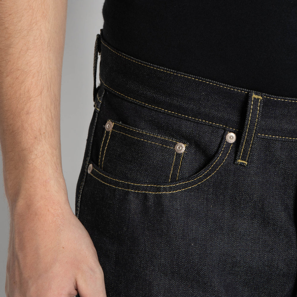 Close-up of a person wearing dark indigo denim jeans with yellow contrast stitching, showing the back pocket and waistband area.