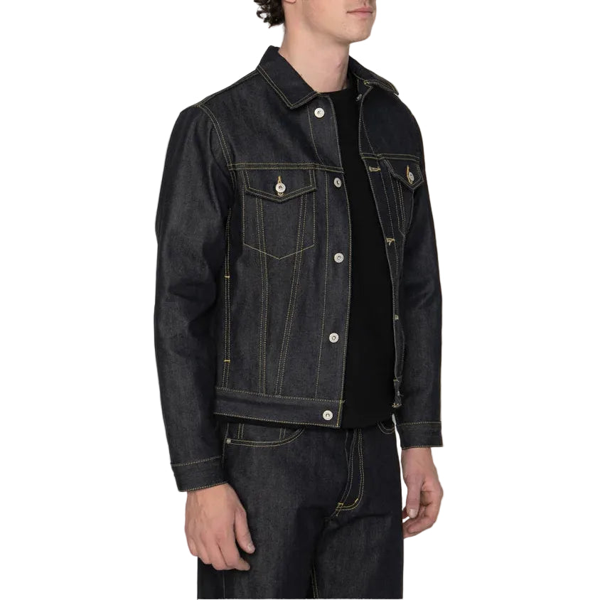 A man wearing a dark indigo denim jacket over a black shirt and matching dark jeans, standing against a plain white background.