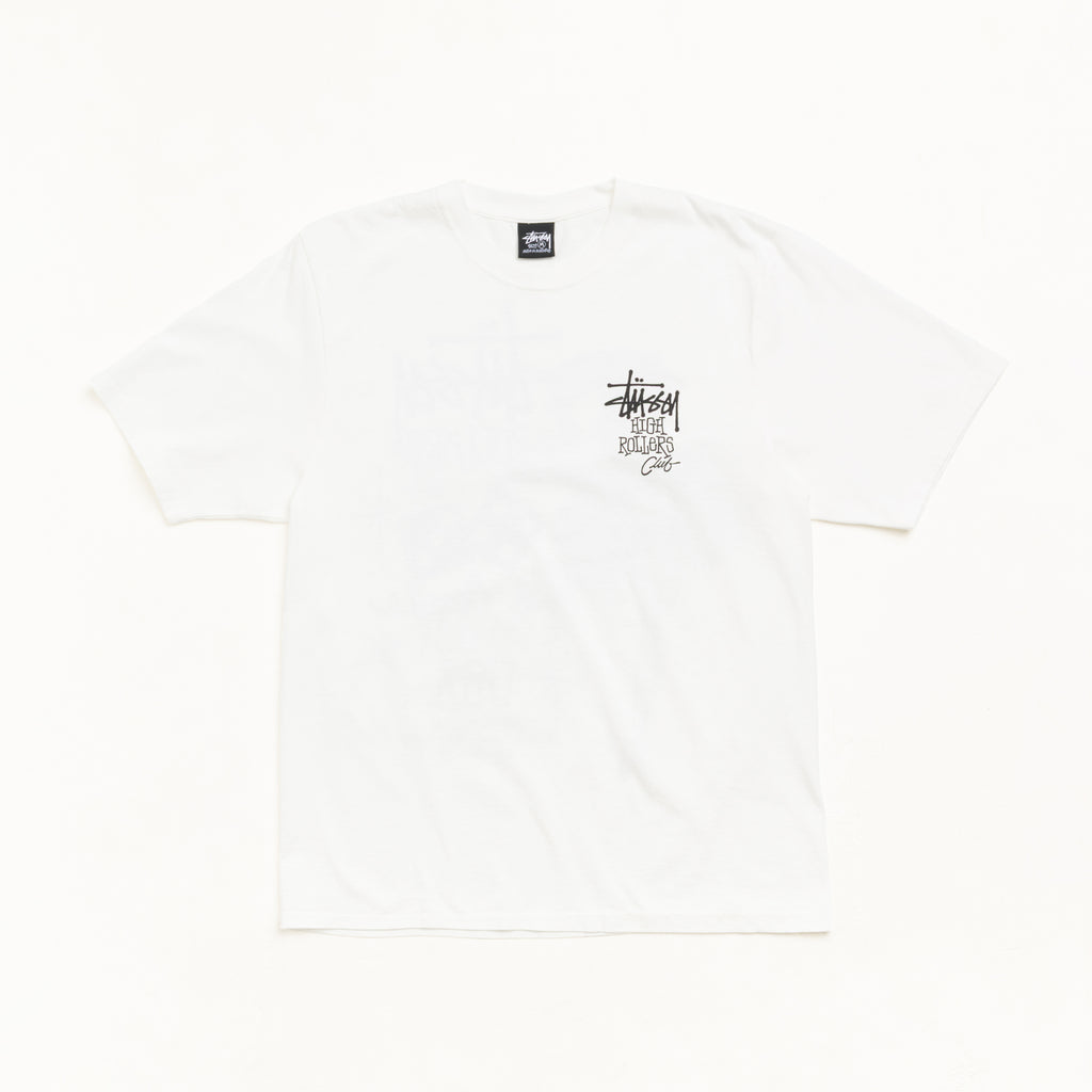A white Stussy short-sleeve t-shirt with a small black and gray graphic on the left chest, laid flat against a clean white background.