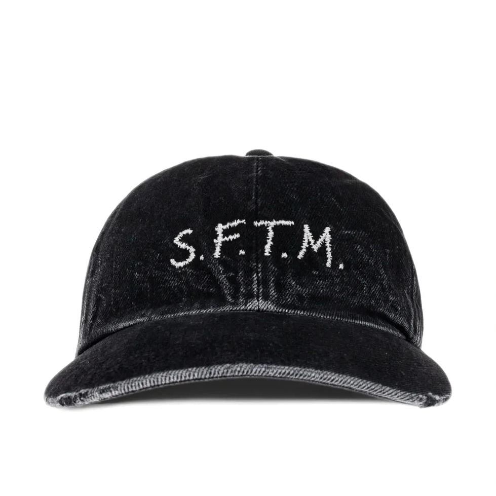 Front view of the Song For The Mute SFTM Cap, a washed black denim baseball cap with “S.F.T.M.” embroidered in off-white across the front.