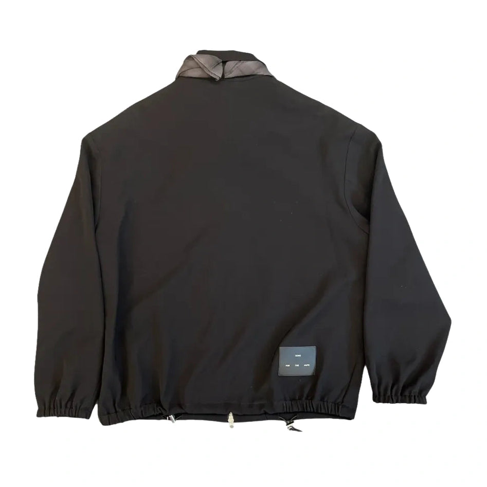 Back view of the black Slim Coach Jacket laid flat, showing the gray neckerchief at the collar, elastic cuffs, the drawcord hem and a “Song For The Mute” label patch on the lower back.