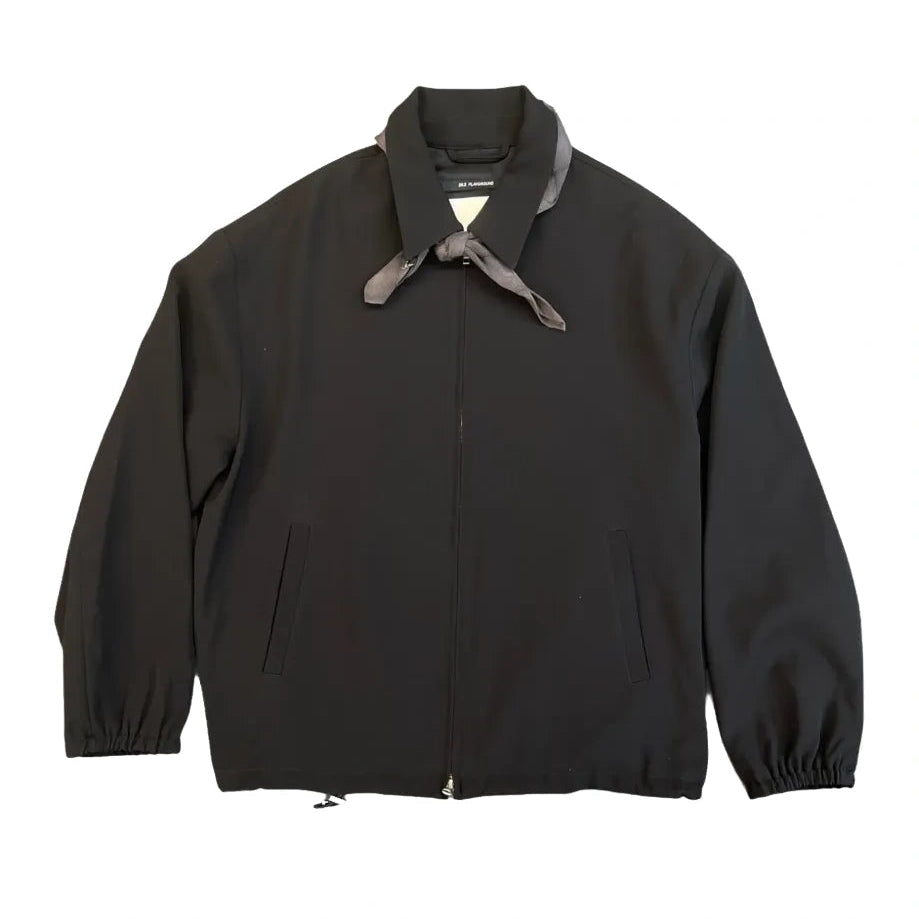 Front view of the Song For The Mute Slim Coach Jacket laid flat. A black zip-front jacket with a point collar, a gray neckerchief knotted at the neck, welt pockets and elastic cuffs.