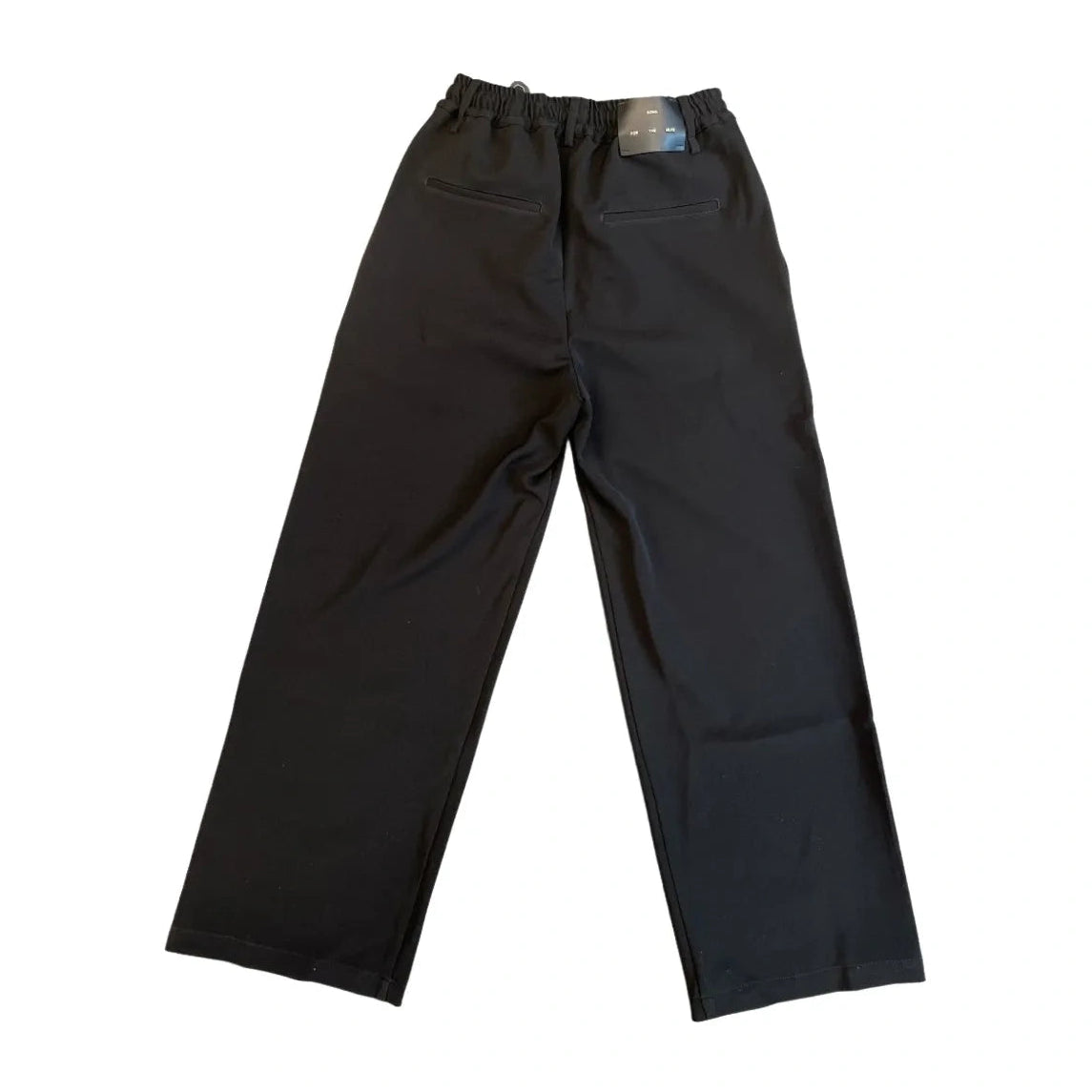 Back view of the black wide-leg pants laid flat, showing two welt pockets and a “Song For The Mute” label patch on the elastic waistband.