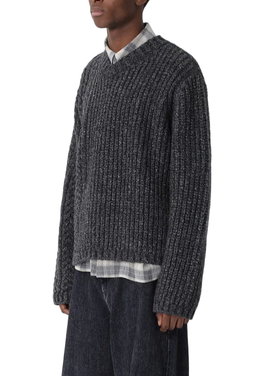 Man wearing a dark textured sweater and wide-leg jeans on a white background