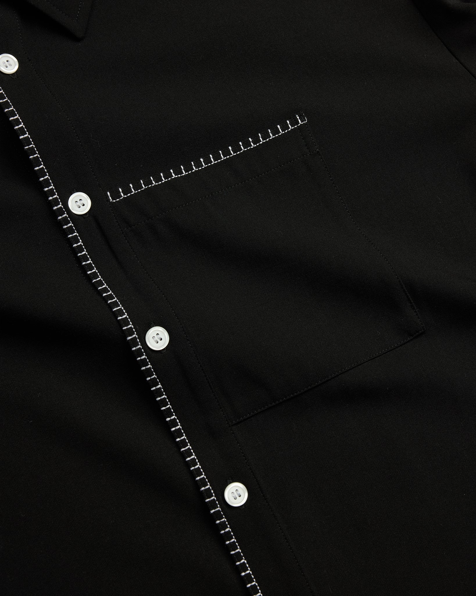 Close-up of a black shirt with white stitching and buttons.