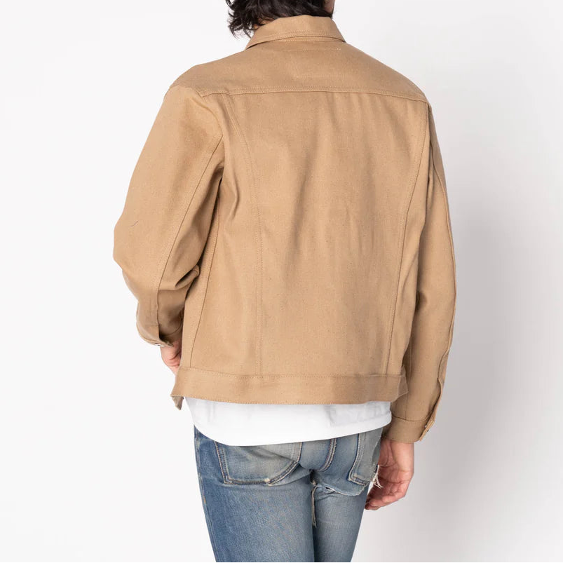 Person wearing a beige jacket and blue jeans on a white background