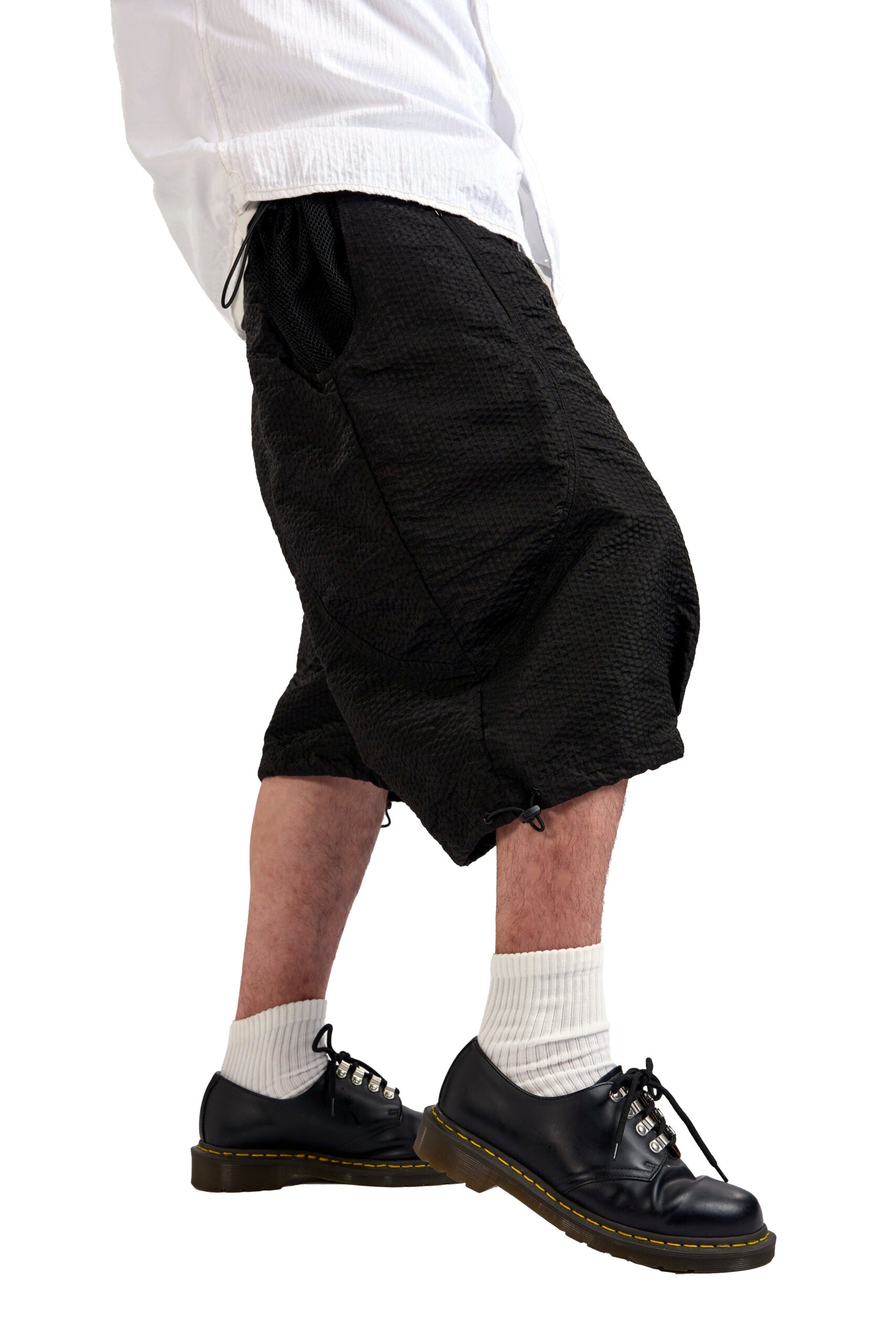 Person wearing black shorts, white socks, and black shoes on a white background