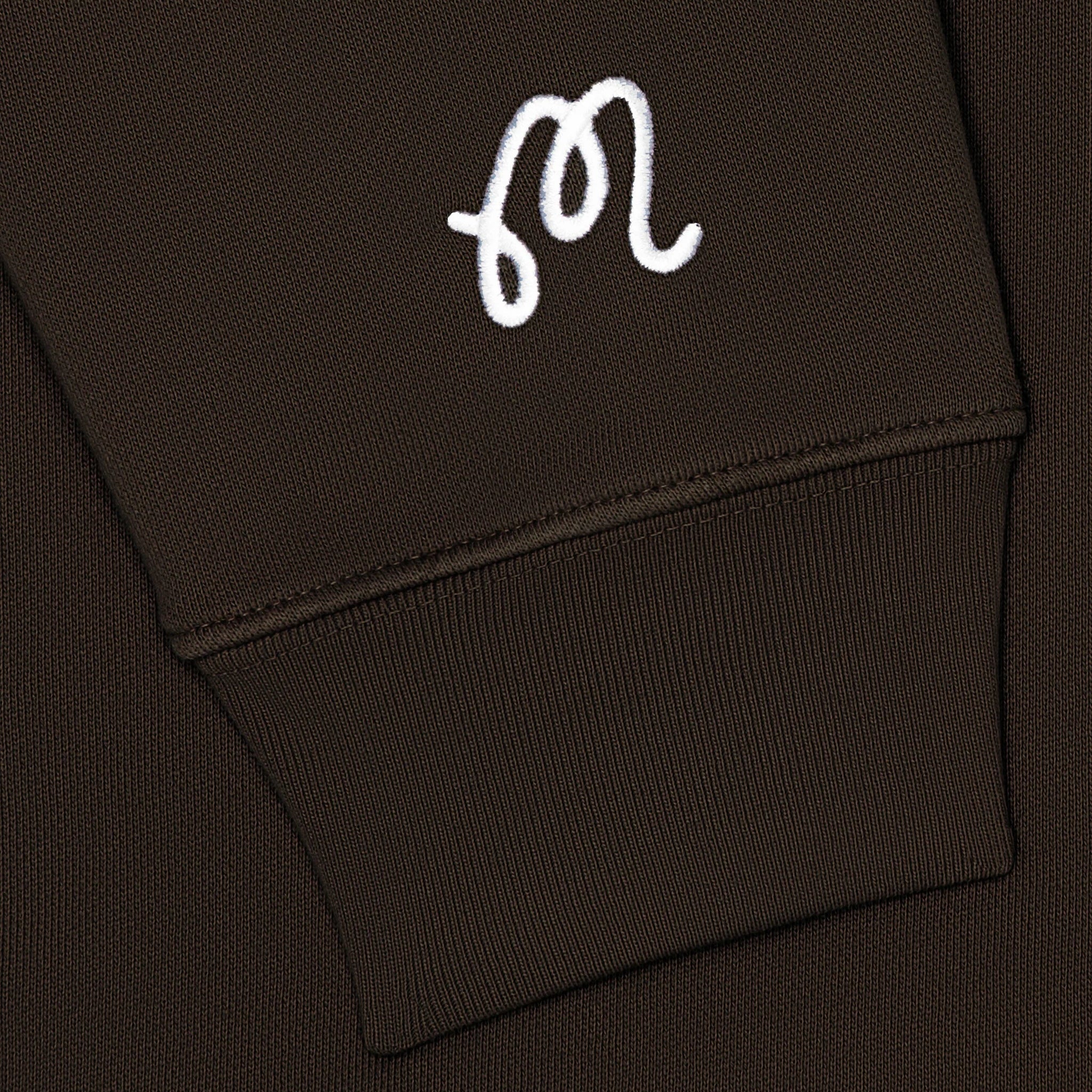 Close-up of a brown hoodie with a white logo on the sleeve.