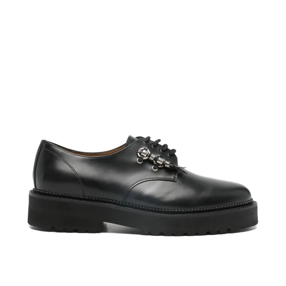 Black leather shoe with decorative brooch on a white background