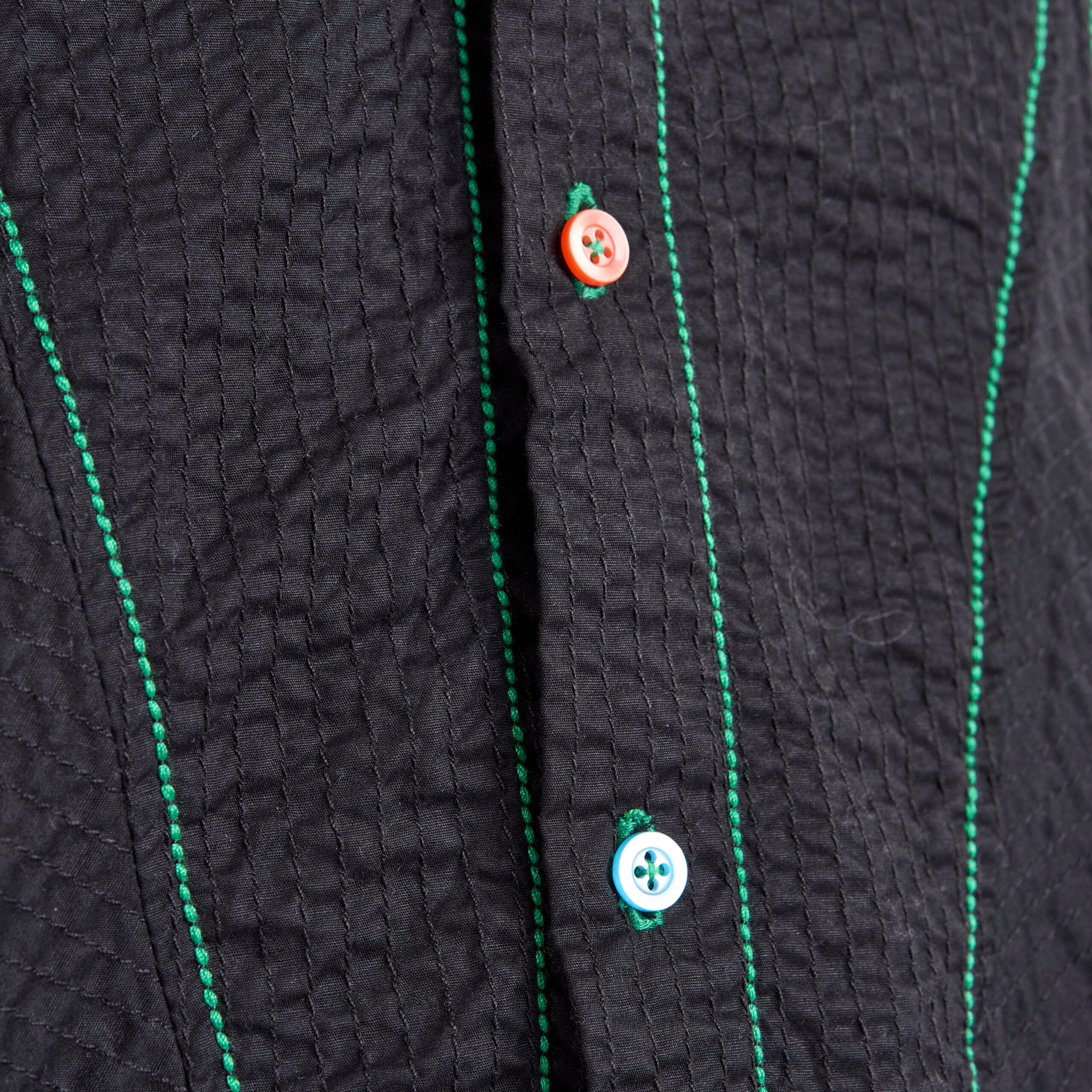 Close-up of a textured black garment with green stitching and buttons.