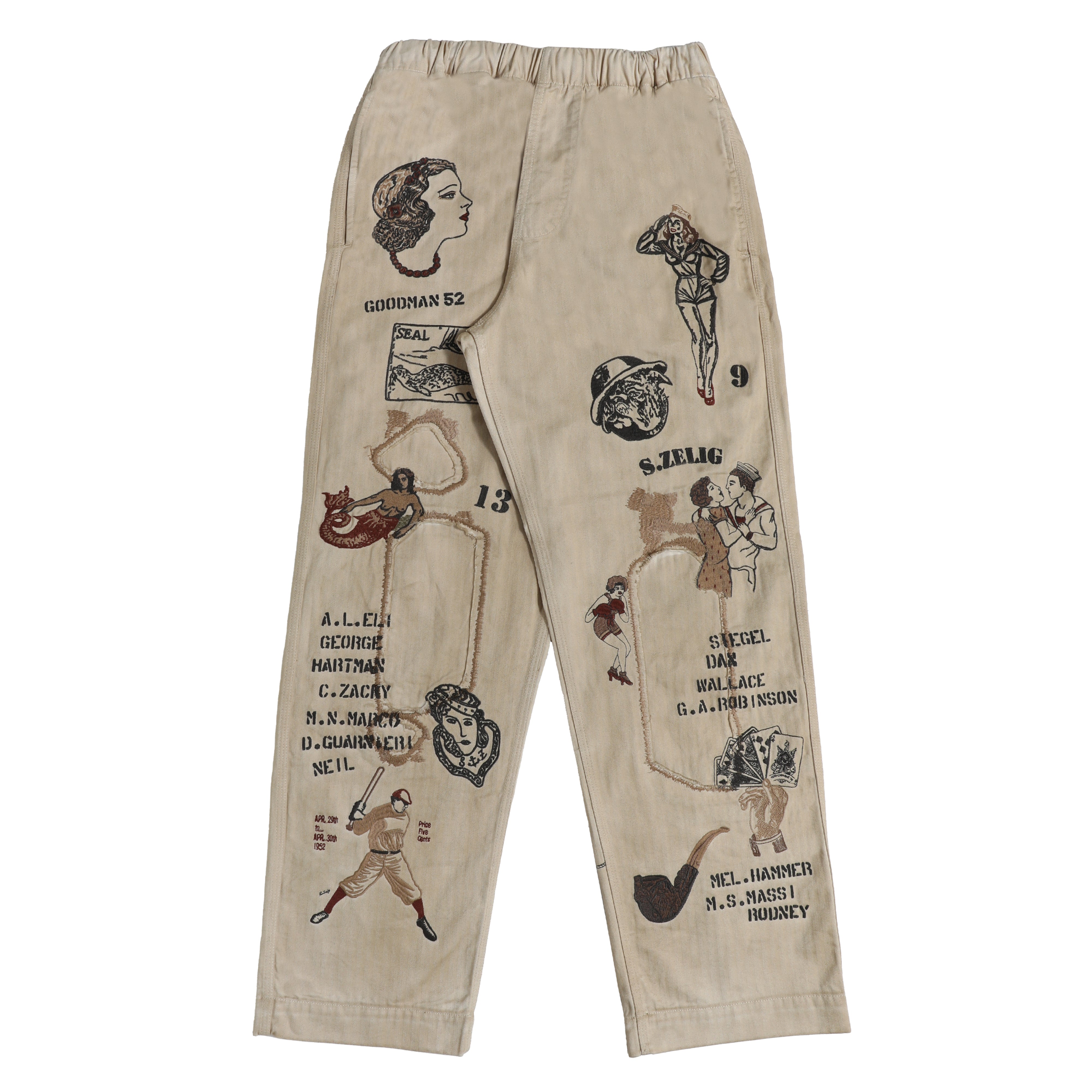 Beige canvas cargo pants featuring vintage-style embroidered illustrations and text on both legs, including pin-up girl graphics and names