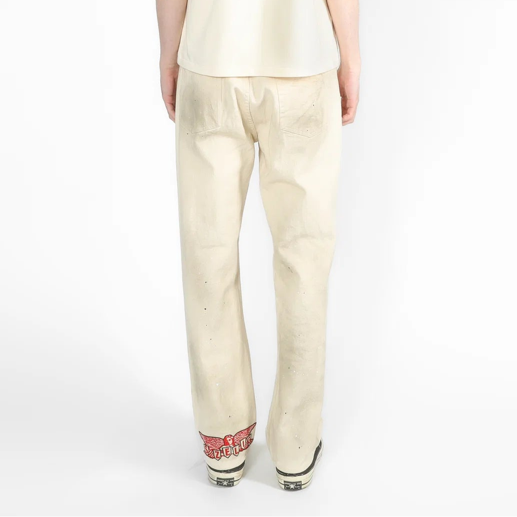 A model viewed from the back, wearing a cream-colored shirt and matching cream trousers, standing against a plain white studio background.