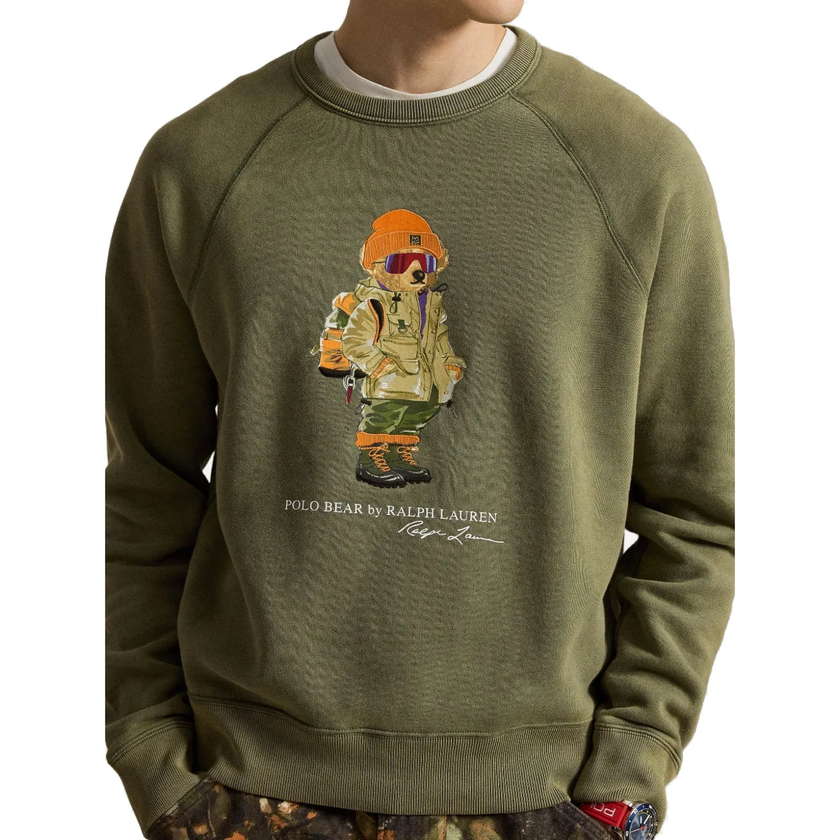 Close-up of the Polo Bear graphic on the Red Rock Crewneck: a bear in an orange beanie, ski goggles, a khaki parka, camo pants and boots, with “Polo Bear by Ralph Lauren” below.