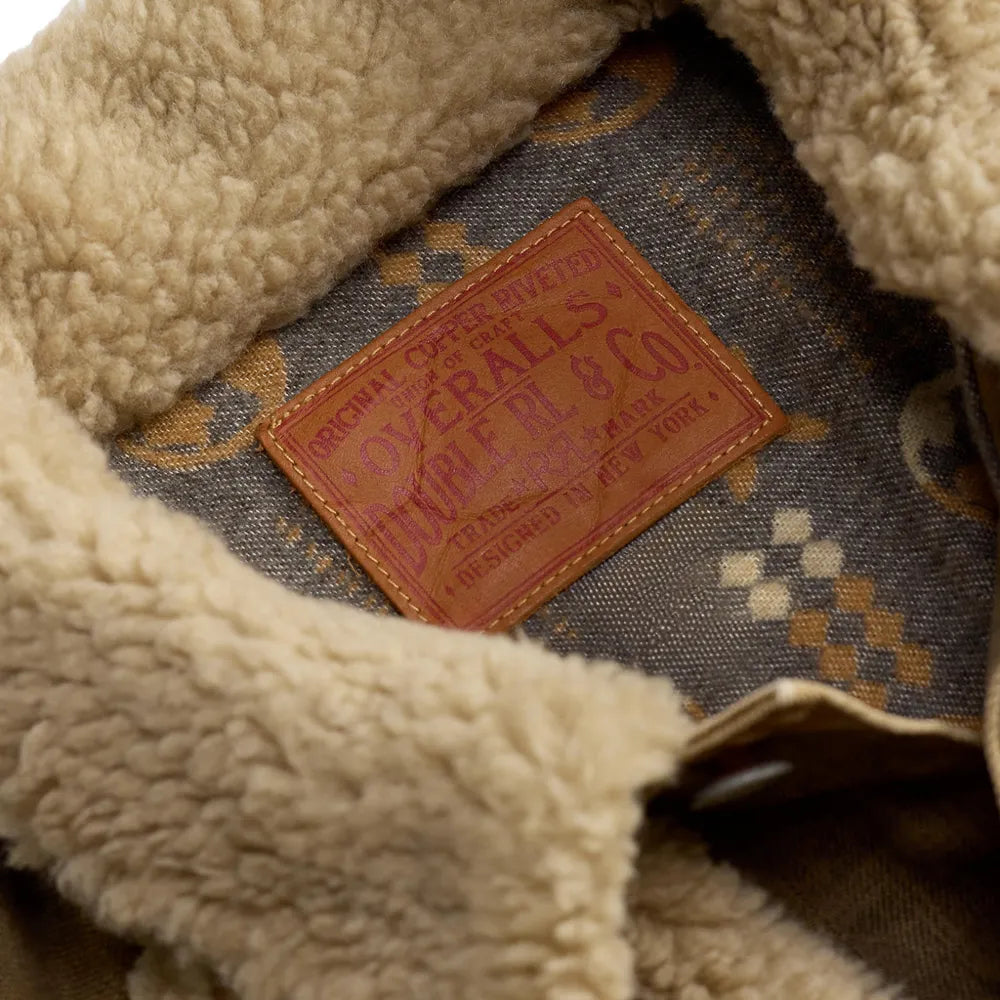Close-up of a beige sherpa fleece collar and lining of a vintage work jacket, showing a brown leather patch with 'Overalls Double RL Co.' branding.