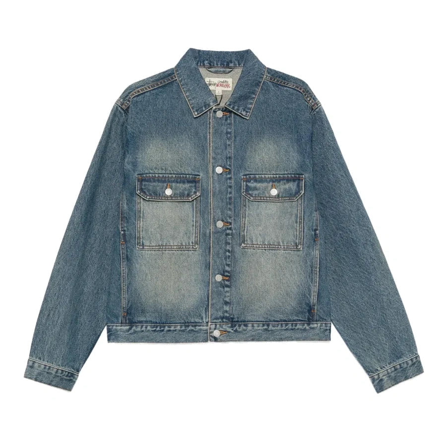 Front view of the Stüssy Trucker Denim jacket in dark wash indigo laid flat. A faded, vintage-washed denim jacket with silver buttons and two flap chest pockets.