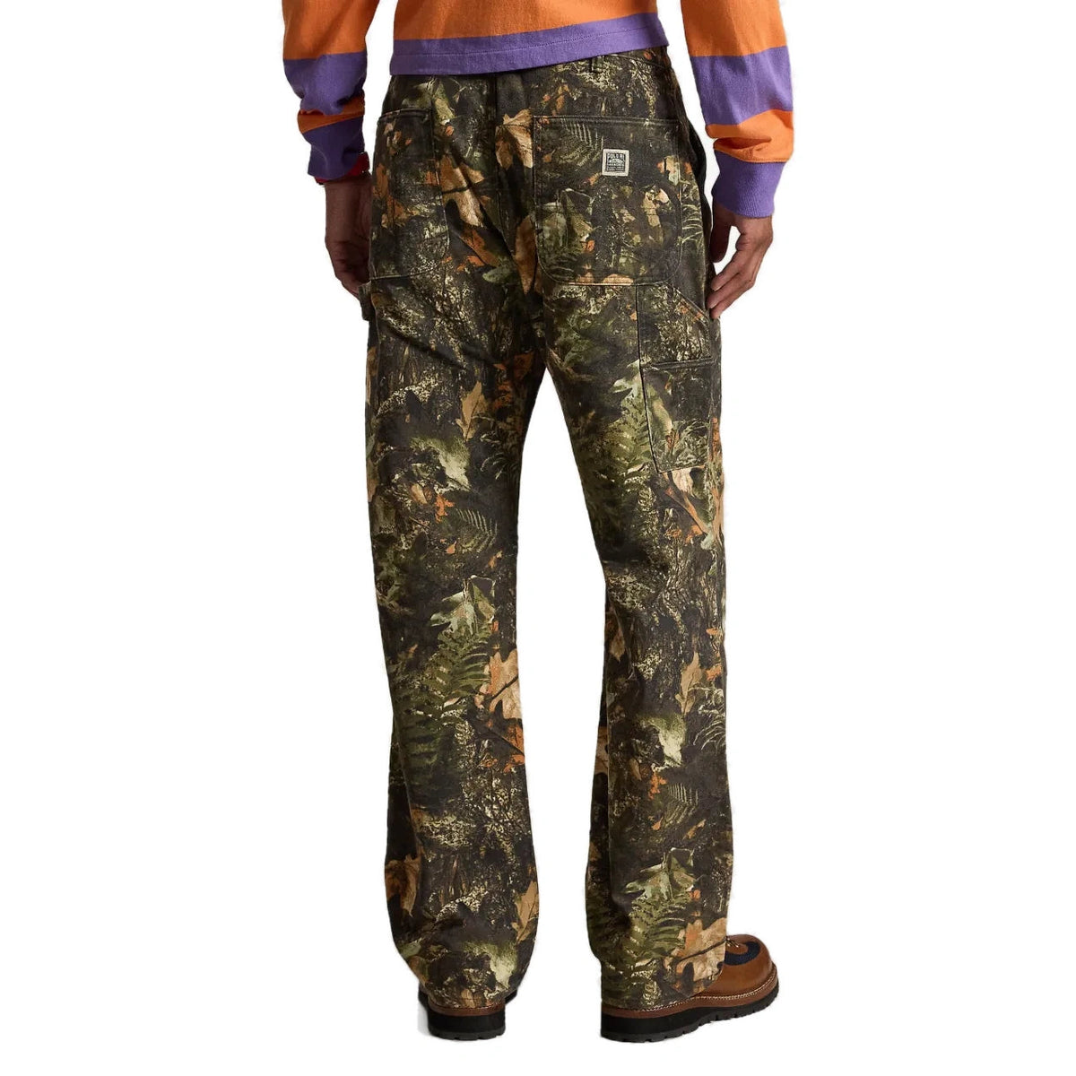 Back view of the forest-print pant on a model, showing the back patch pockets with a Polo patch and the side utility pocket, worn with brown boots.