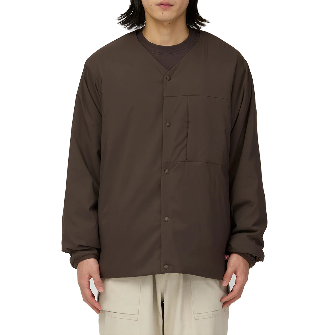 Model wearing the dark brown Snow Peak Flexible Insulated Cardigan fully snapped over a brown crewneck top, with light beige pants, showing the relaxed fit and chest pocket.