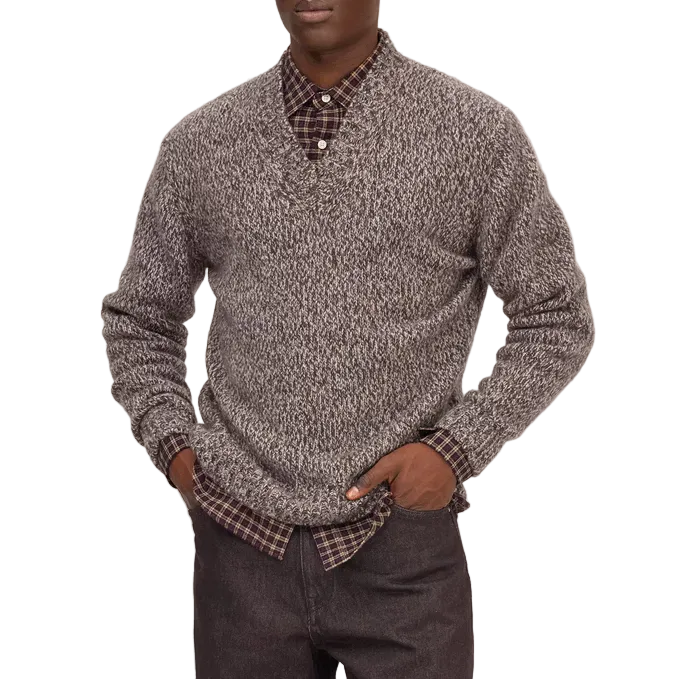 A man modeling a gray and black marled knit sweater over a patterned collared shirt, paired with dark brown trousers and black shoes, against a white background.