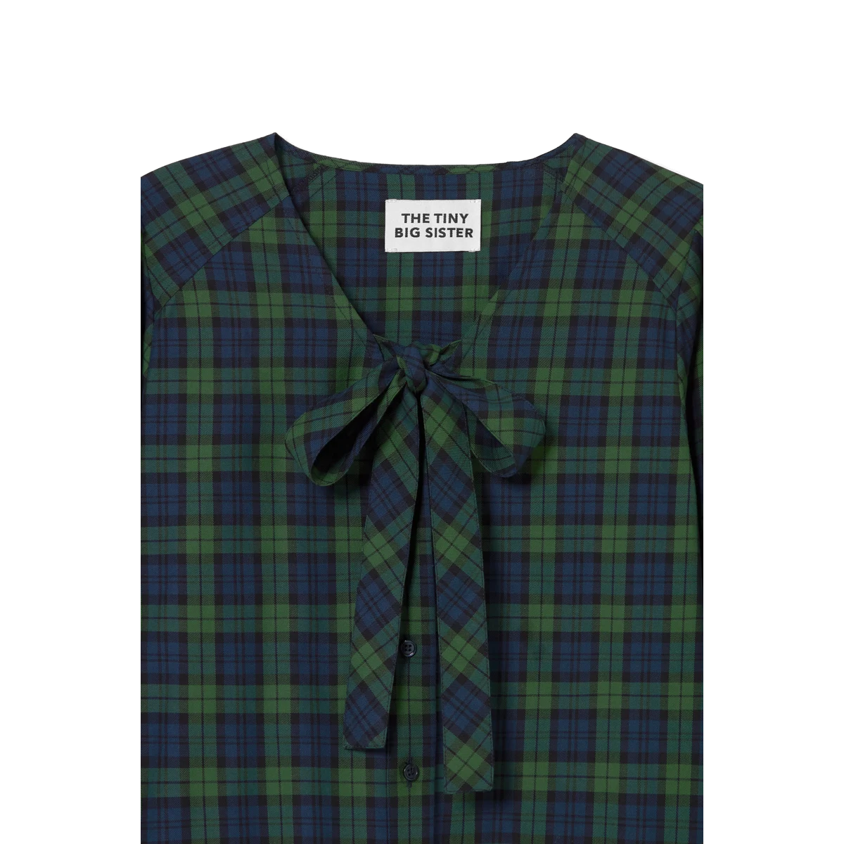 Close-up of the V-neck on The Tiny Big Sister Green Check Bow Blouse, showing the self-fabric bow, navy buttons and brand label.