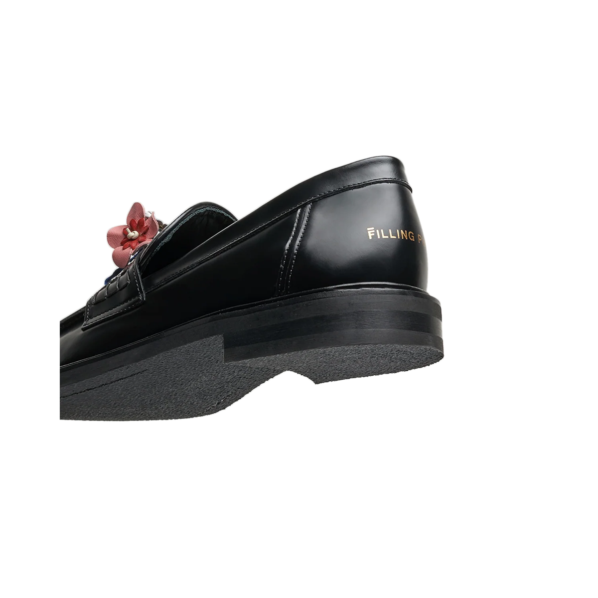 Rear three-quarter view of a black Filling Pieces loafer, showing the gold logo on the heel, the stacked heel, and the textured rubber sole.