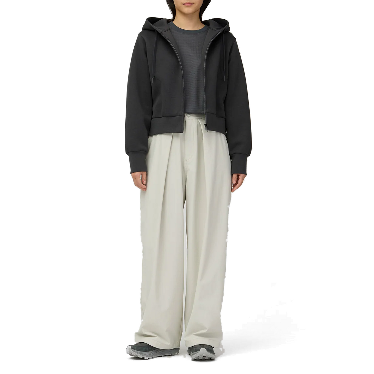 Full-length view of a model wearing the charcoal Snow Peak Odor Control Women’s Zip Parka open over a grey top, with off-white wide-leg pleated pants and grey trail shoes.