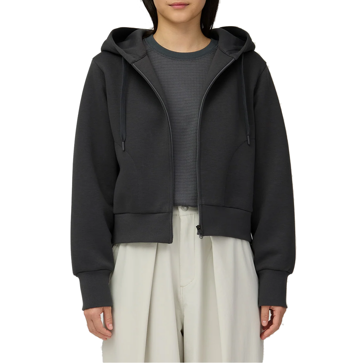 Waist-up view of a model wearing the charcoal Snow Peak Odor Control Women’s Zip Parka unzipped, showing the cropped length, drawstring hood and ribbed cuffs.
