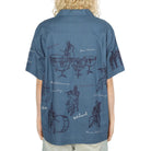 Person wearing a blue shirt with black graphics on the back, standing against a white background