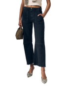Person wearing faded black jeans and a white top, holding a small bag on a plain background