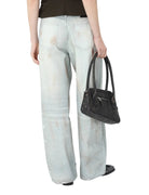 Person wearing light blue jeans and holding a black handbag on a white background