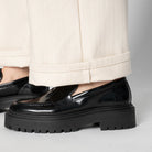 Black platform loafers worn with beige pants on a neutral background