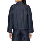 Person wearing a dark denim jacket and pants on a white background