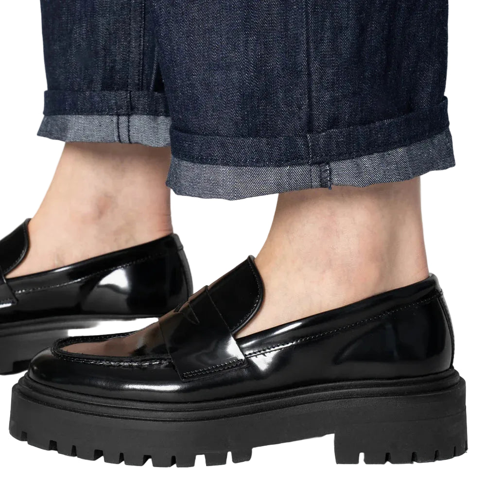 Black loafers worn with rolled-up jeans on a neutral background