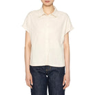 Woman wearing a beige shirt and dark jeans on a white background
