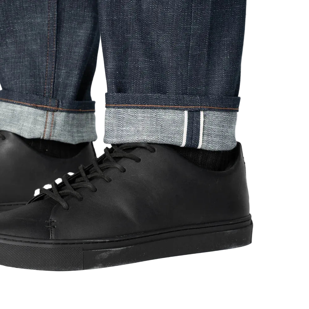 Black shoes worn with rolled-up jeans on a plain background
