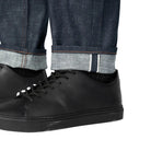 Black shoes worn with rolled-up jeans on a plain background