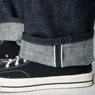 Close-up of dark blue jeans with rolled-up cuffs and black sneakers on a light gray background