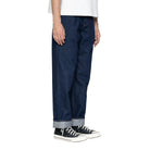Person wearing dark blue jeans and black sneakers on a white background