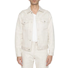 Person wearing a light-colored denim jacket over a white shirt and pants on a plain background