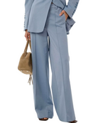 Person wearing a light blue suit with wide-leg pants holding a brown handbag on a white background